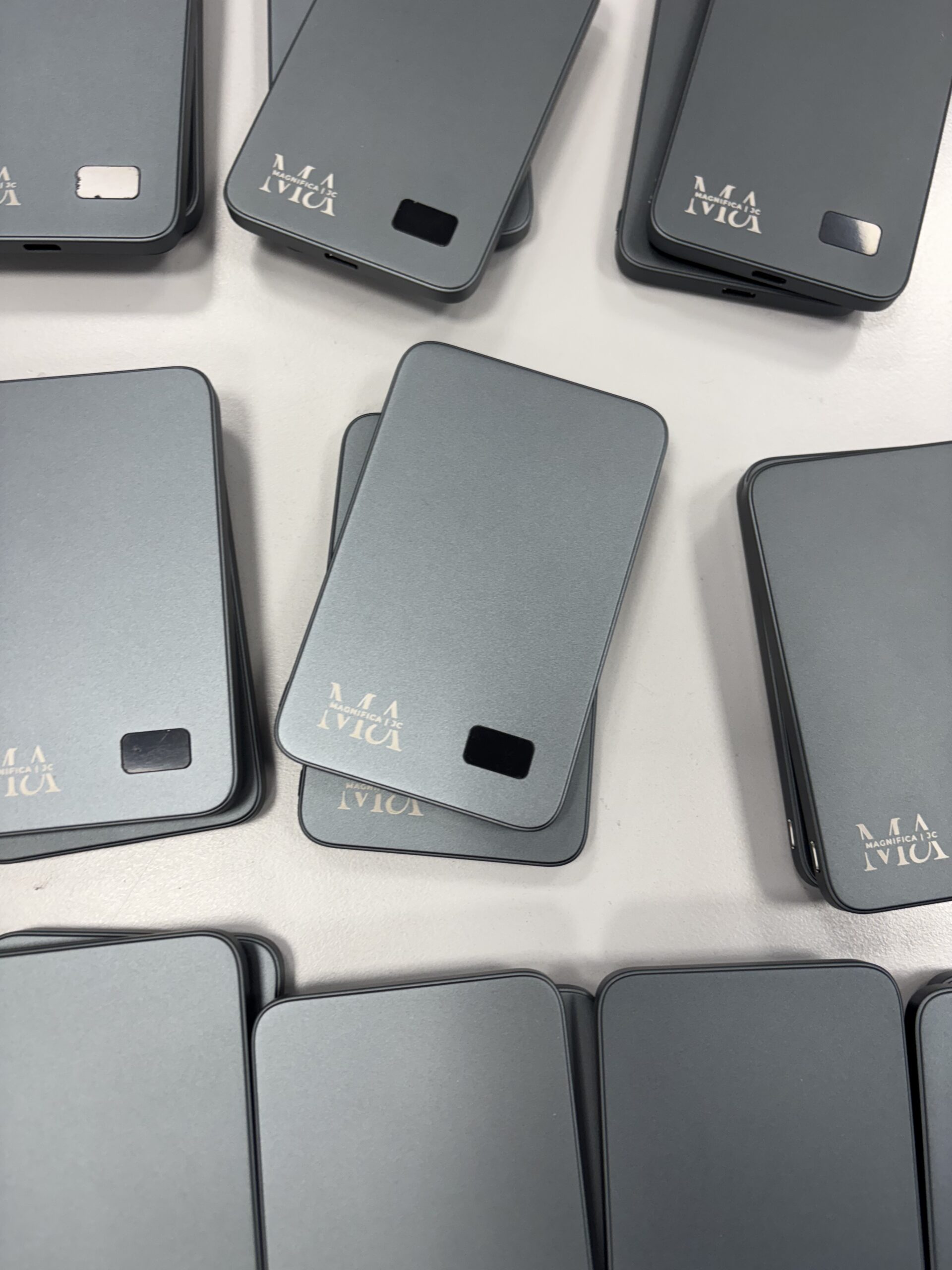 Multiple Magnifica powerbanks arranged on a table showing their uniform gray finish and logo.